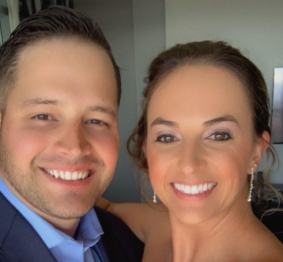 Brian and Kaci are taking a selfie together. Brian is wearing a blue shirt and Kaci is wearing a strapless dress.