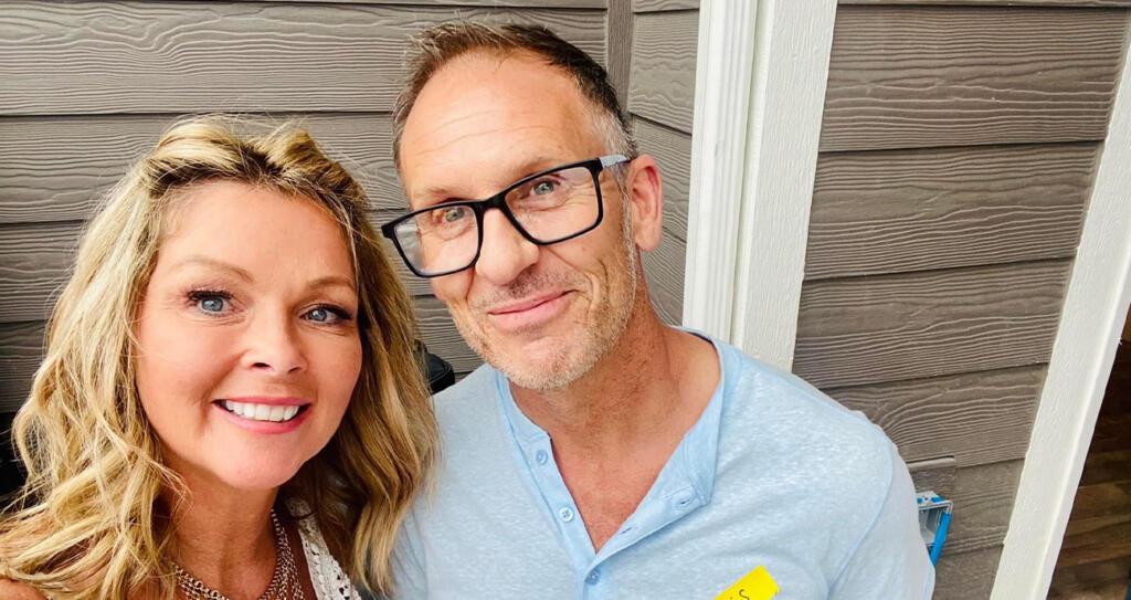 Helen and Chris are standing together, posing for a photo. Chris is wearing a blue shirt and both are smiling at the camera.